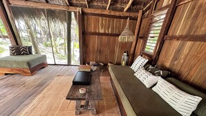 A wooden-floored living area with a green sofa, a wooden coffee table, and a red-fringed rug. - Rancho Sarah Tulum in Sian Ka’an  (Tulum)