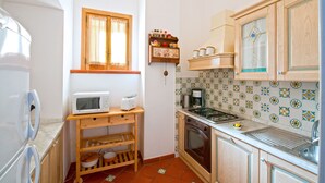 Cocina compacta con microondas, tostadora, estufa y pileta. Hay un estante de madera con vajilla y una ventana sobre la pileta.