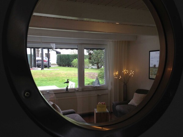 Ein Zimmer mit einem Rundfenster, einem Sessel, einem kleinen Tisch und einer Vase mit Lichterkette.