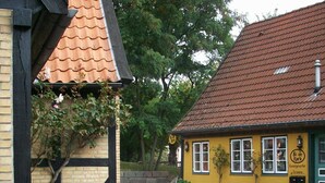 Ein gelbes Gebäude mit einem Ziegeldach, einem Kopfsteinpflasterhof und umgebender Bepflanzung.