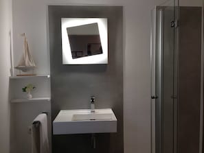 Un baño con lavamanos blanco, espejo y puerta de ducha de vidrio.
