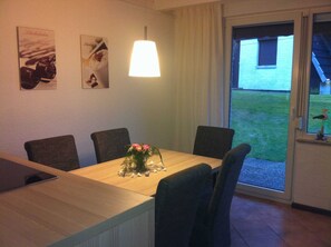 Ein Essbereich mit Tisch, Stühlen, einer Lampe und Blick auf ein Haus und eine Rasenfläche.