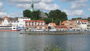 Eine Stadt am Wasser mit historischen Gebäuden, einem markanten Kirchturm und einem rot-weißen Boot, das an der Anlegestelle liegt.