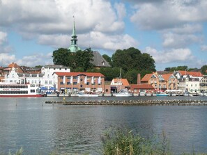 A waterfront town with historic buildings, a prominent church spire, and a red and white boat docked at the pier. - Cottage bunk with Schleiblick (Kappeln)