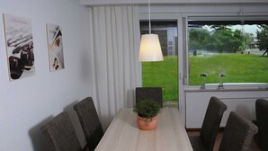 Ein Essbereich mit Tisch, Stühlen, einer Pendelleuchte, einem Blumentopf und Blick durch ein Fenster.