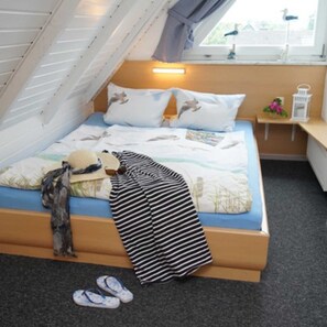 A bedroom with a sloped ceiling, a bed with a striped blanket, pillows with animal prints, a nightstand with a lamp, and a window with a view of buildings.