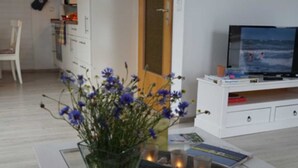 A modern living room with a white TV stand, a glass vase with flowers, and a magazine on the table. - Apartment De lütte Stove - Apartment Woydt De lütte Stove (Kappeln)