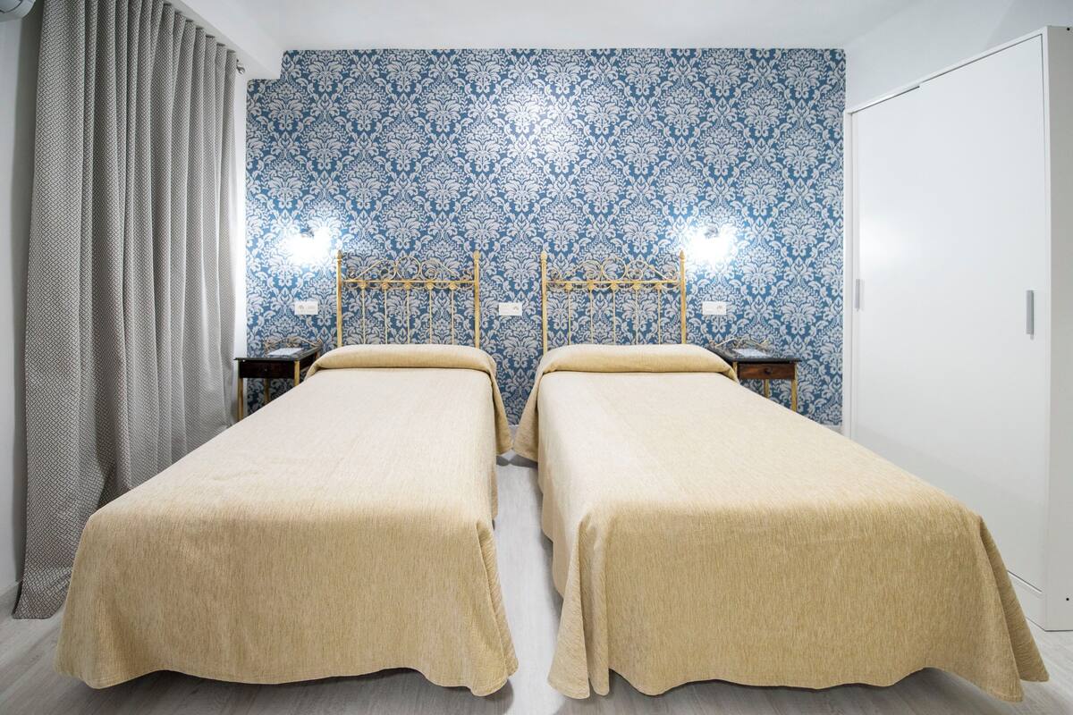 A twin room with two beds, a patterned wallpaper, and a curtain.