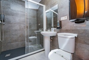Een moderne badkamer met een douchecabine van glas, een witte wastafel en een toilet.