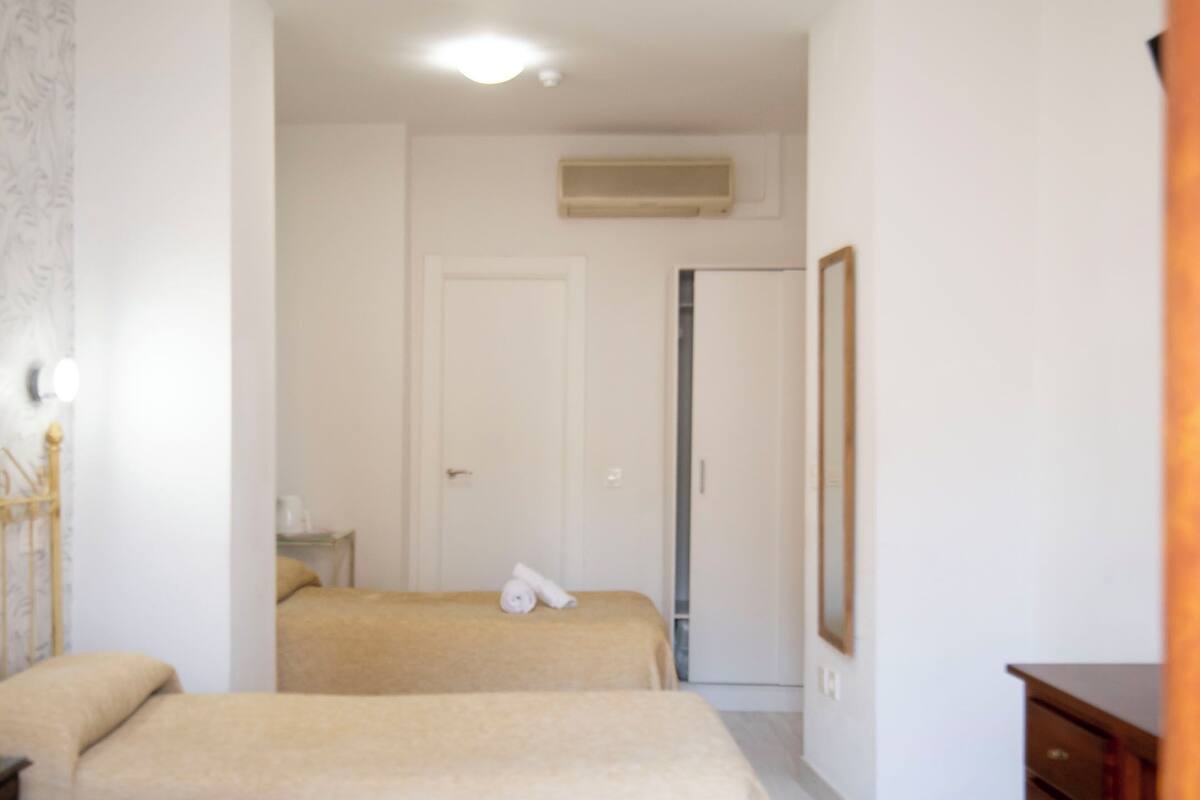 A room with two beds, a wooden dresser, a mirror, and a door leading to another room.