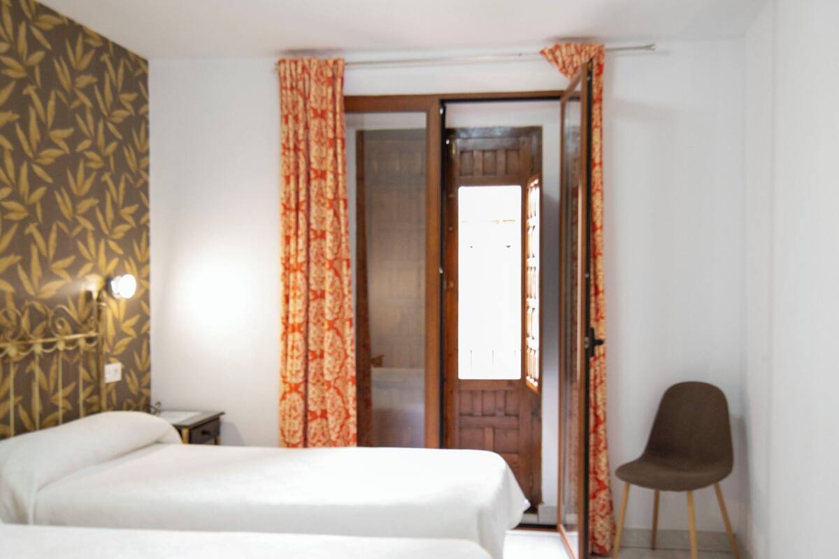 A hotel room with two beds, a chair, a nightstand, and a door leading to a bathroom.