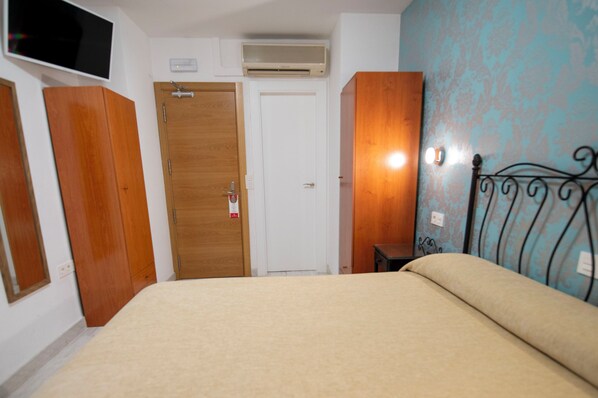 A bedroom with a bed, wooden wardrobe, a white door, and a wall-mounted air conditioner. - Hotel Manzanito (Antequera)