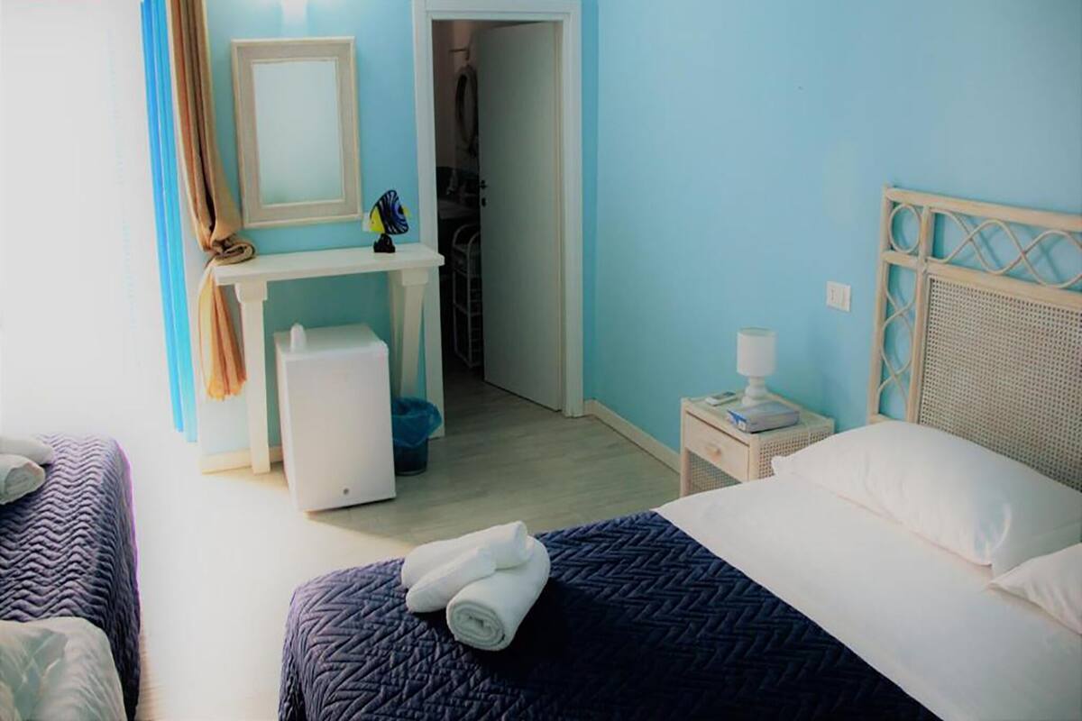 Habitación de hotel con dos camas, un escritorio con espejo, una mesita de noche con lámpara y un armario.