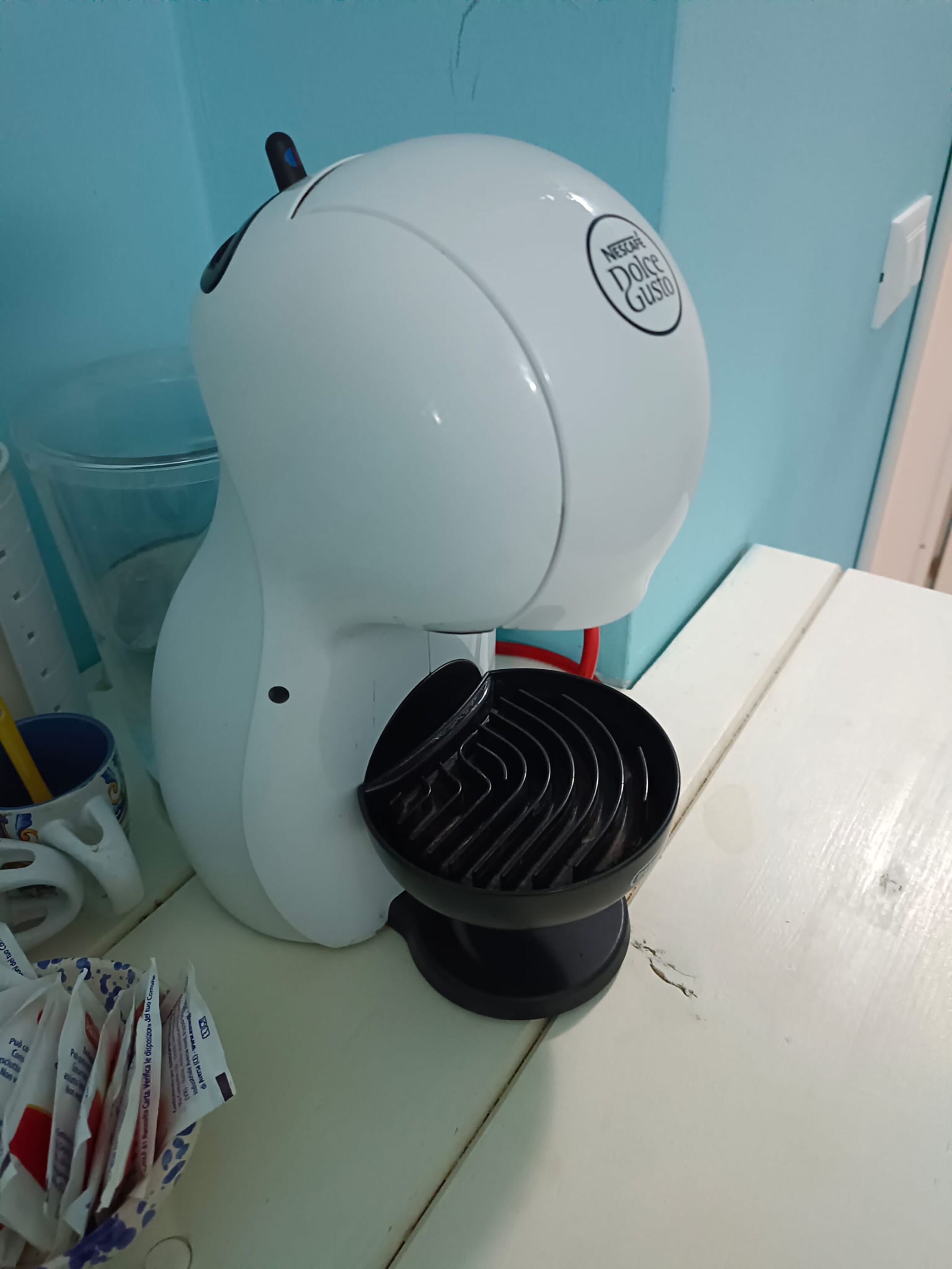 Eine weiße Kaffeemaschine mit einem schwarzen Abtropfbehälter auf einem weißen Tisch.