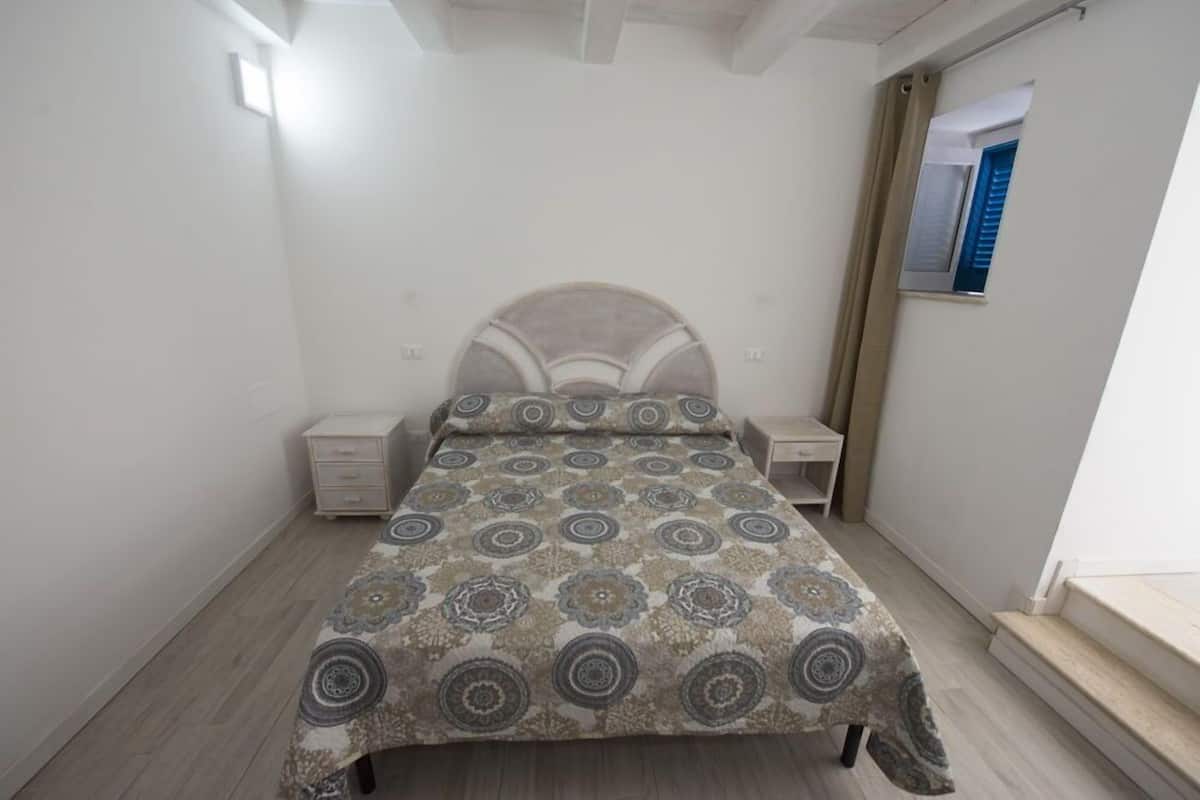 Un dormitorio con cama, mesitas de noche y una ventana con contraventanas azules.