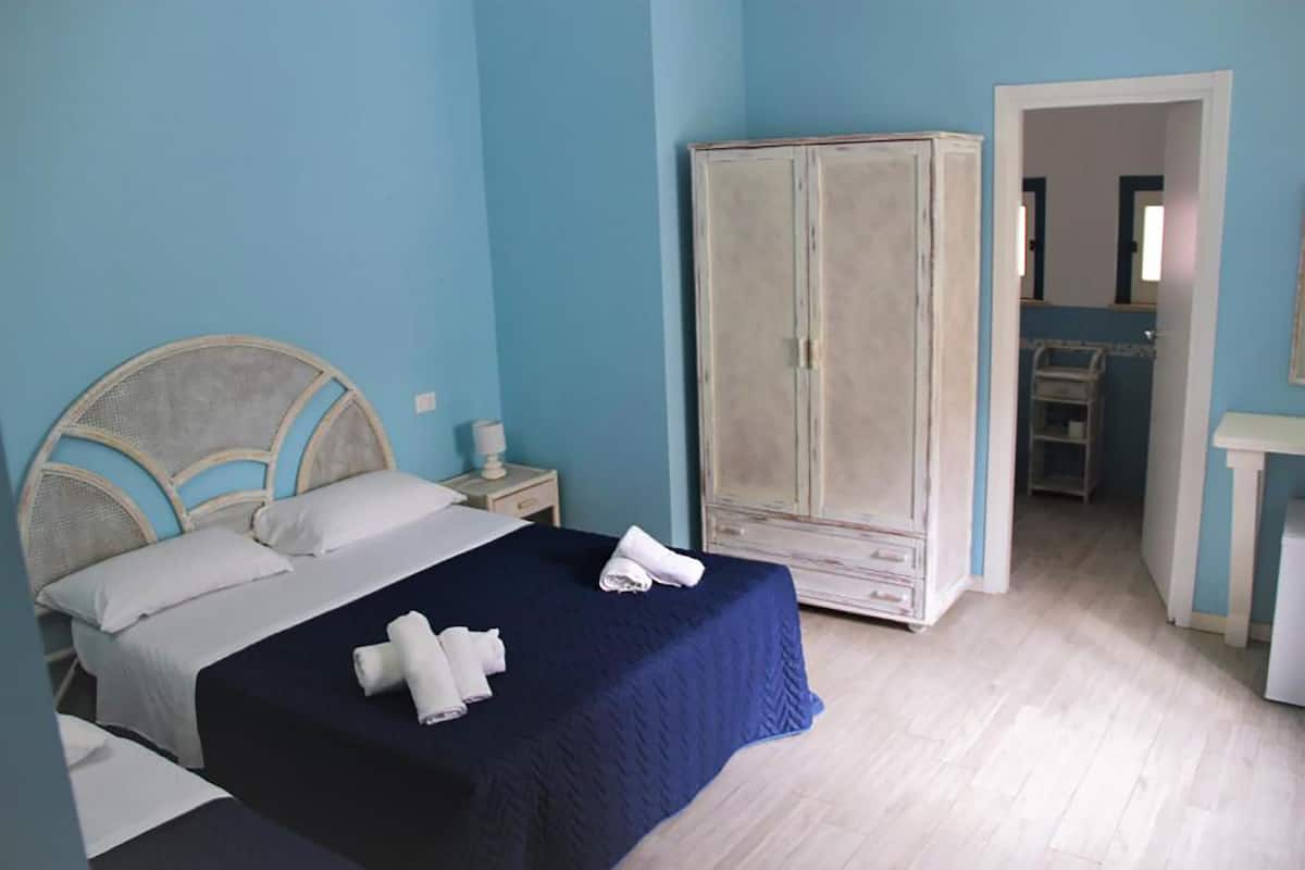 Un dormitorio con cama, armario, mesita de noche y baño visible a través de una puerta abierta.