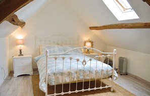 A bedroom with a sloped ceiling, a bed with a white metal frame, a nightstand with a lamp, and a window with a view.