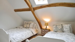 Une chambre avec deux lits simples, une table de chevet avec une lampe et des poutres apparentes.