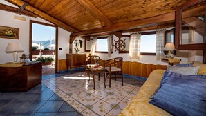 A cozy room with wooden ceiling beams, a bed with blue and yellow bedding, a wooden dresser, and a chair. - Villa Gioiello (Amalfi)