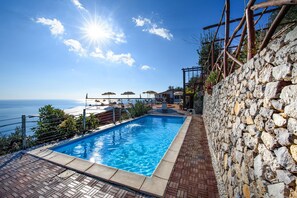 Une piscine avec un mur en pierre et vue sur la mer.