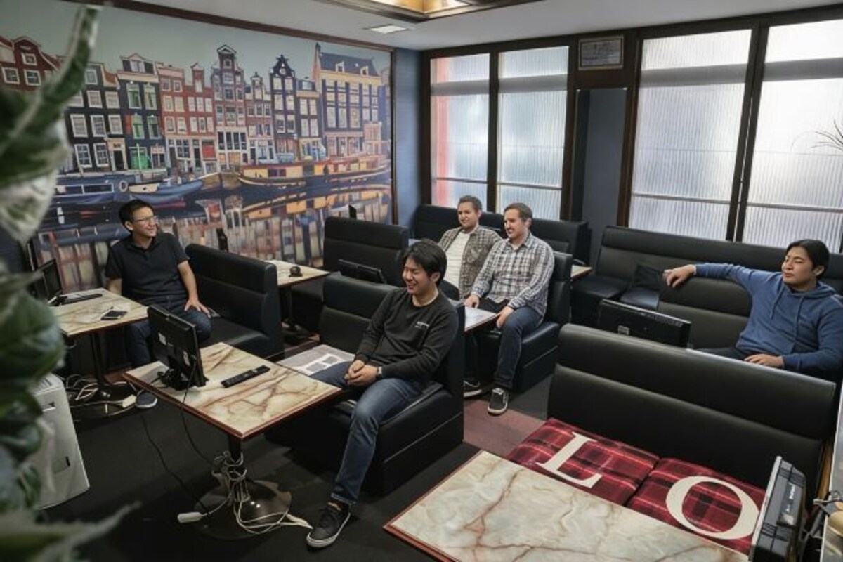 A group of people seated in a modern lounge area with a cityscape mural, comfortable seating, and a large window.