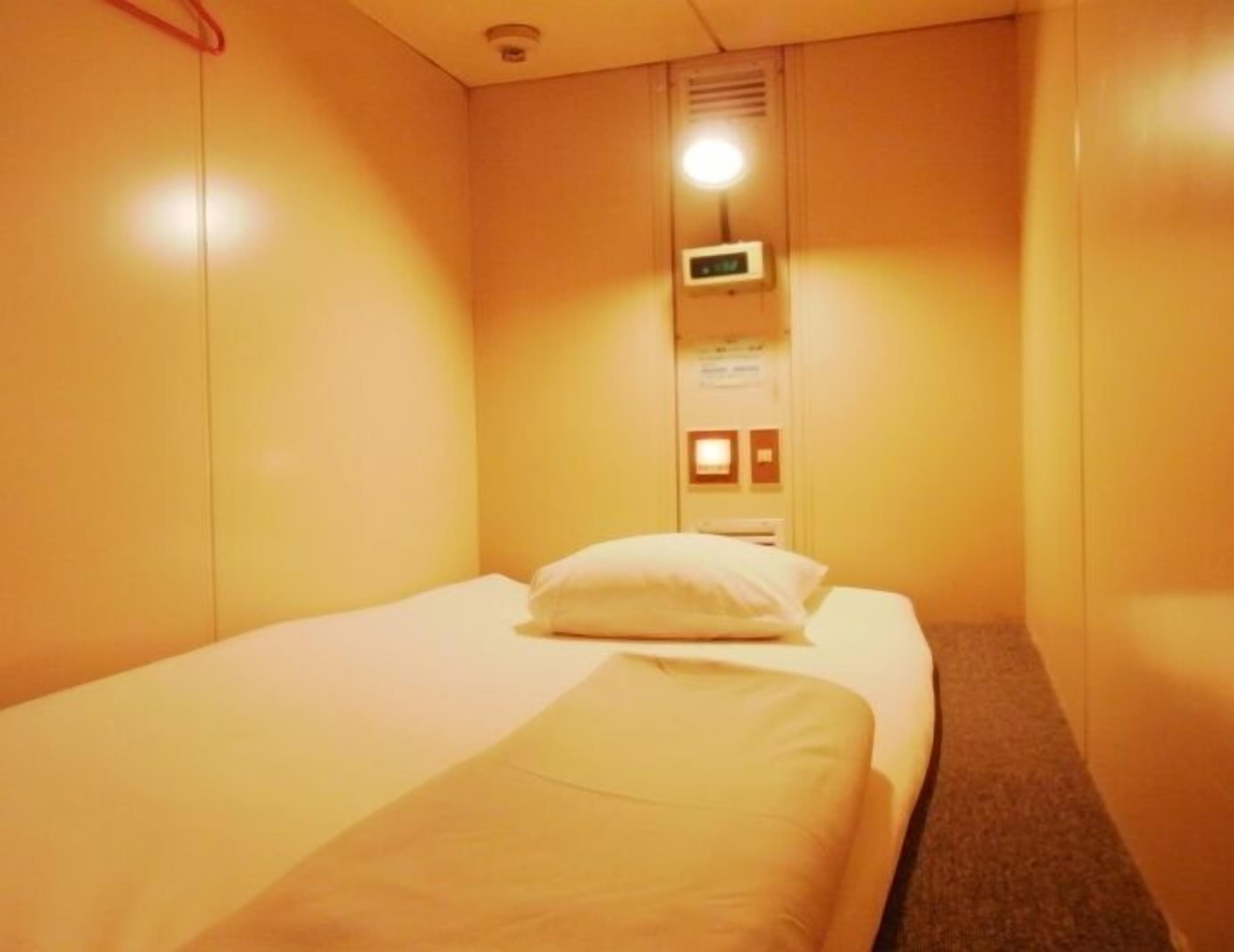 A small, single-bed room with a bed, a wall-mounted control panel, and a door.