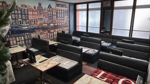 Un restaurant avec des banquettes en cuir noir, des tables surmontées de marbre et une fresque murale représentant un paysage urbain.