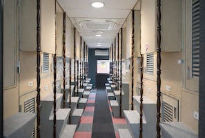 A hotel hallway with lockers, a checkered carpet, and a door at the end. - Capsule Hotel Block Room (Tokyo)