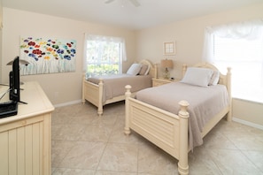 A bedroom with two beds, a desk, a lamp, and a painting on the wall. - Sunside House, 3/2 Pool Home in Gated Community and minutes from everything. (Naples)