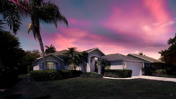 A two-story house with a garage, surrounded by well-maintained lawns and palm trees. - Sunside House, 3/2 Pool Home in Gated Community and minutes from everything. (Naples)