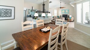 A dining area with a wooden table and chairs, a kitchen in the background, and a living area with a TV and artwork. - Sunside House, 3/2 Pool Home in Gated Community and minutes from everything. (Naples)