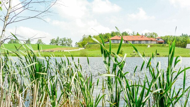 A house with a red roof, surrounded by a grassy area and a body of water. - Nice studio in Borcz with kitchen (Borcz)