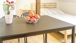 A room with a bed, a table with a basket of apples, a chair, a lamp, and a vase with flowers. - Nice studio in Borcz with kitchen (Borcz)