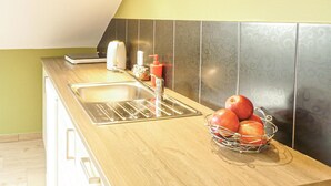 A kitchen with a stainless steel sink, a kettle, a coffee maker, and a fruit basket containing apples. - Nice studio in Borcz with kitchen (Borcz)