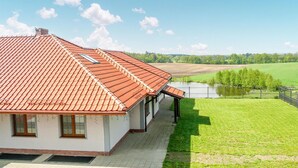 A house with a red-tiled roof, a covered porch, and a view of a green field and a body of water. - Nice studio in Borcz with kitchen (Borcz)