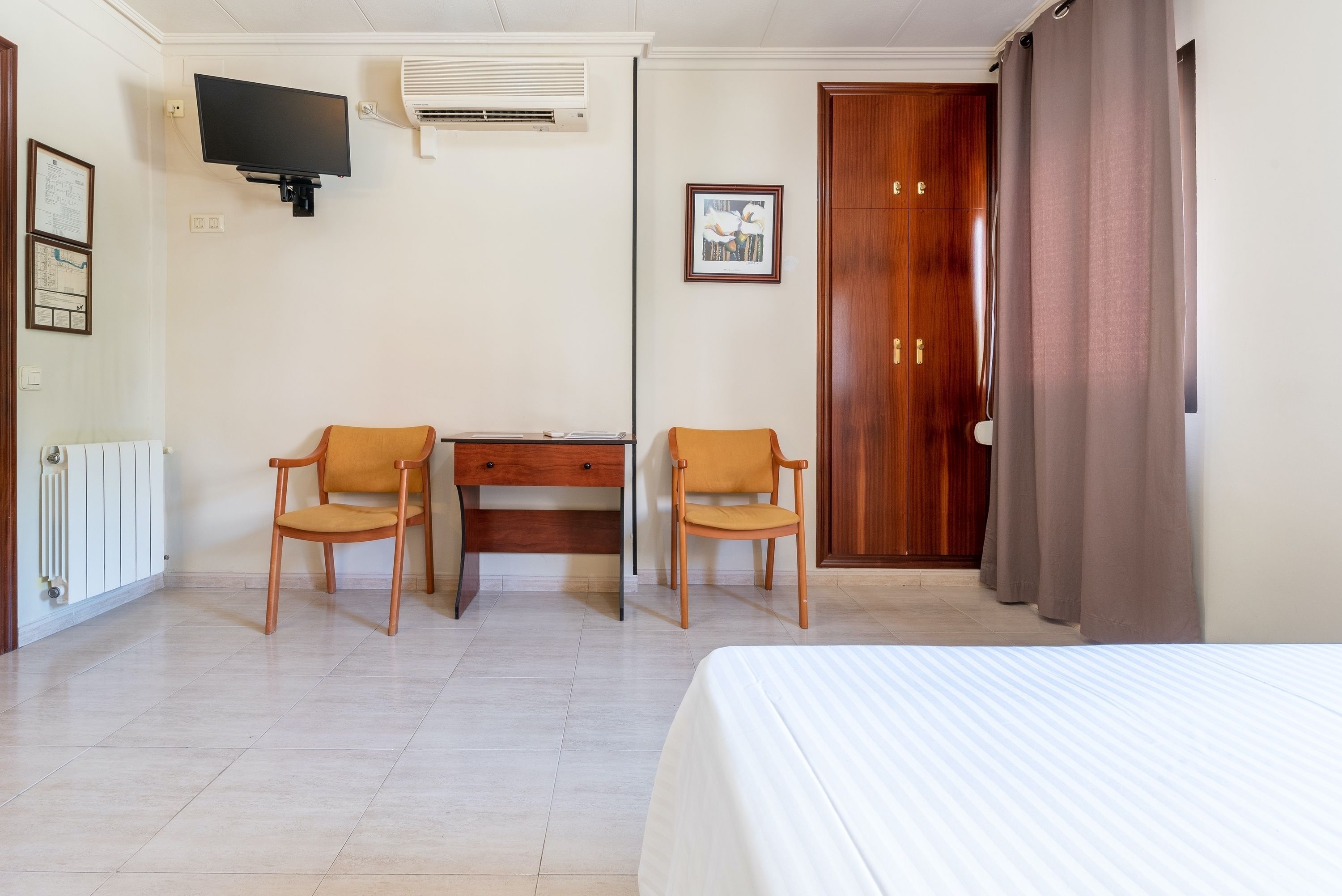A hotel room with a bed, two chairs, a desk, a television, and a wardrobe.