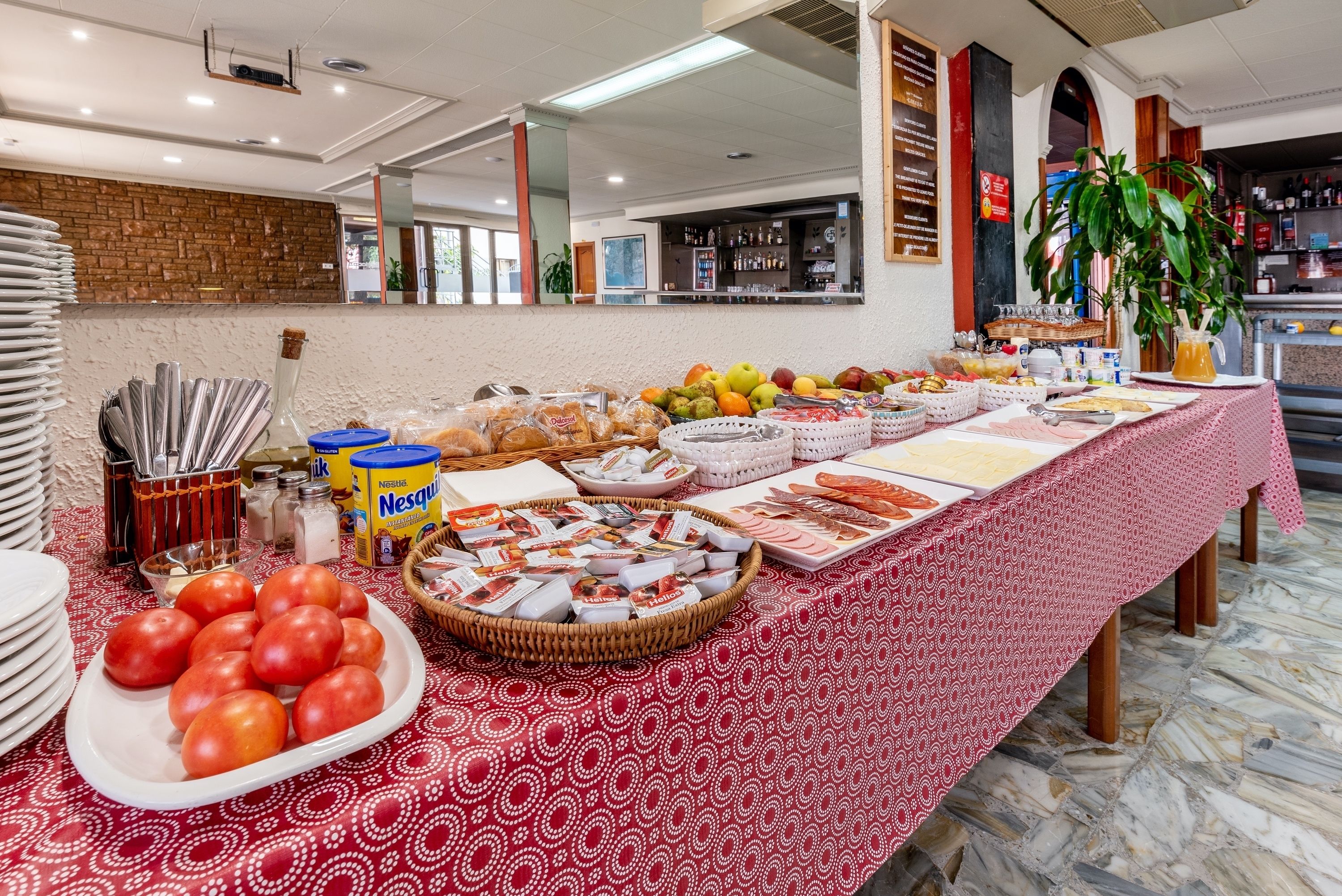 Una mesa de buffet con diversos alimentos y condimentos, un muro de ladrillo y un área de bar al fondo.