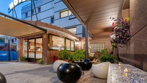 A hotel entrance with a modern facade, outdoor seating area, and potted plants. - Hotel Canadá (Tarragona)