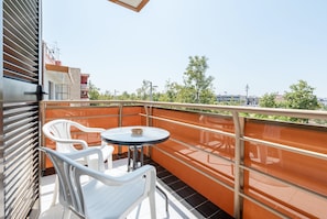 A balcony with a table and chairs, a metal railing, and a view of buildings and trees.
