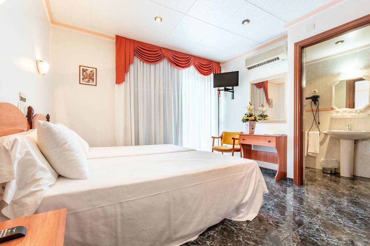 A hotel room with a bed, a desk, a TV, and a bathroom with a sink and mirror.