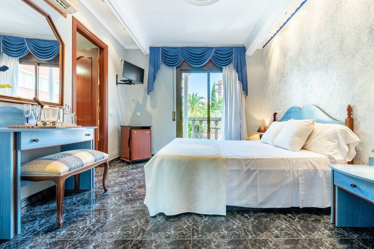 A hotel room with a large bed, a desk with a chair, a mirror, and a view of the outdoors.