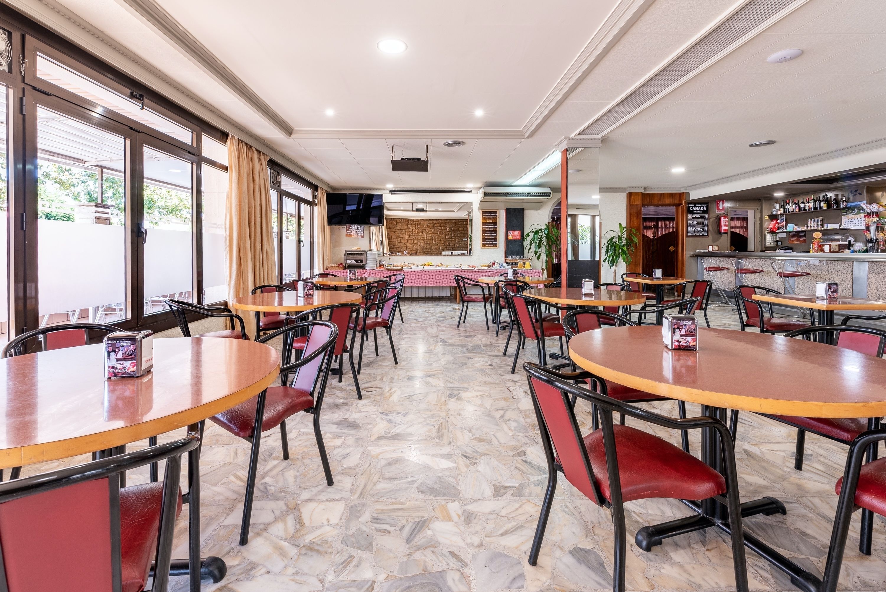 Un restaurante amplio con varias mesas y sillas, una zona de bar y suelo de baldosas de piedra.