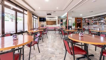Un restaurante amplio con varias mesas y sillas, una zona de bar y suelo de baldosas de piedra.