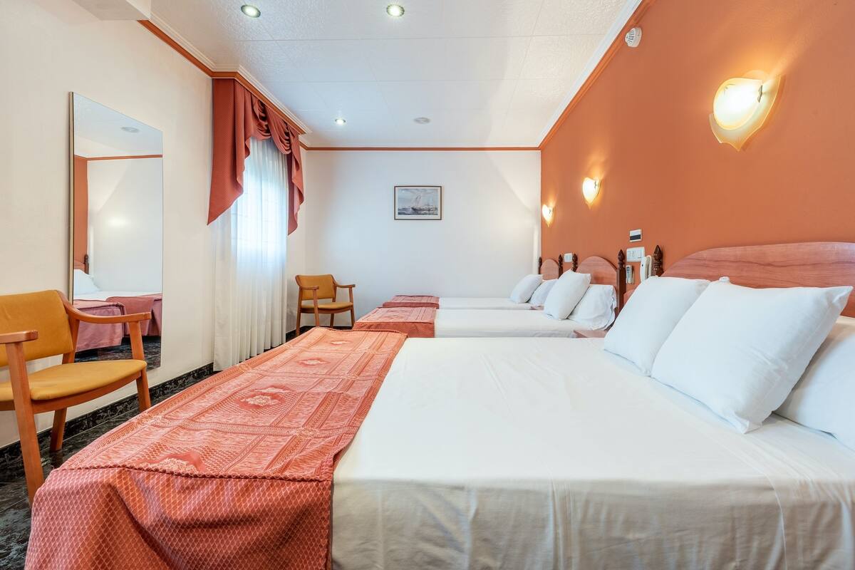 A hotel room with two beds, a large mirror, a wooden chair, and a small table.
