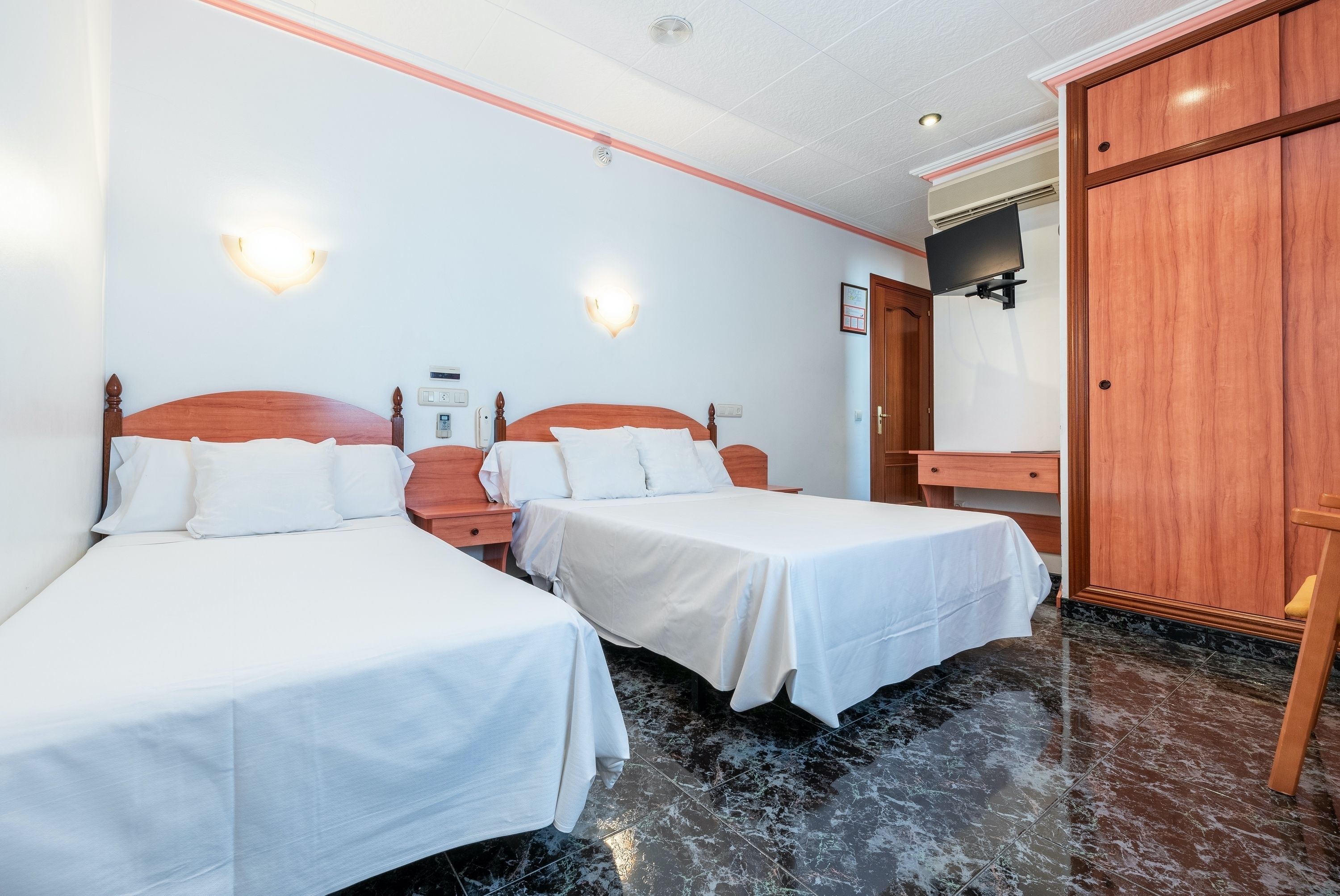 A hotel room with two single beds, a wooden wardrobe, a flat-screen TV, and a marble floor.