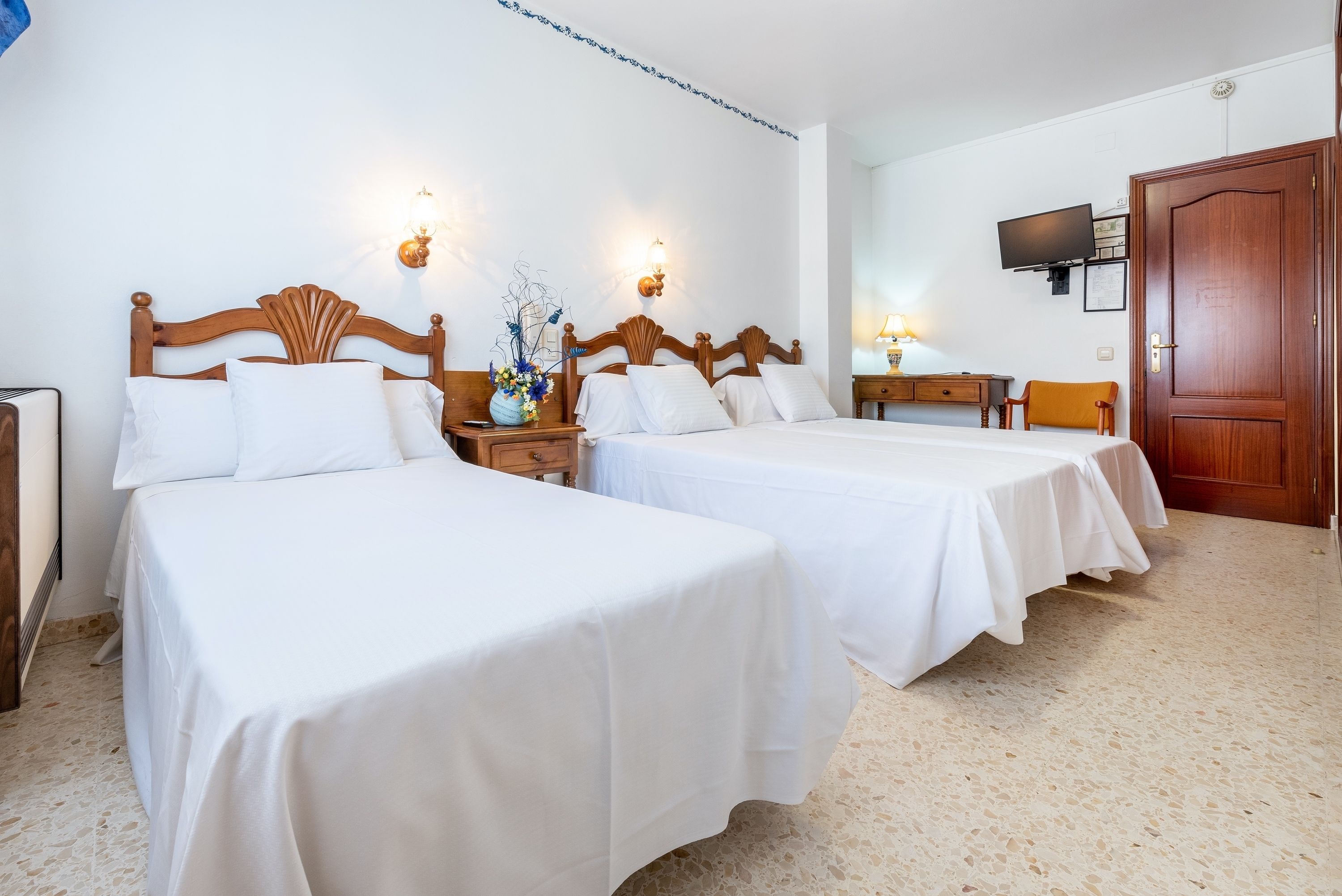 Habitación de hotel con dos camas, un televisor, una puerta de madera y una pequeña mesa con lámpara.