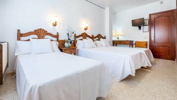 Habitación de hotel con dos camas, un televisor, una puerta de madera y una pequeña mesa con lámpara.