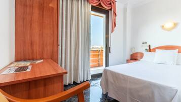 A hotel room with a bed, a desk, a chair, and a view of the outside balcony.