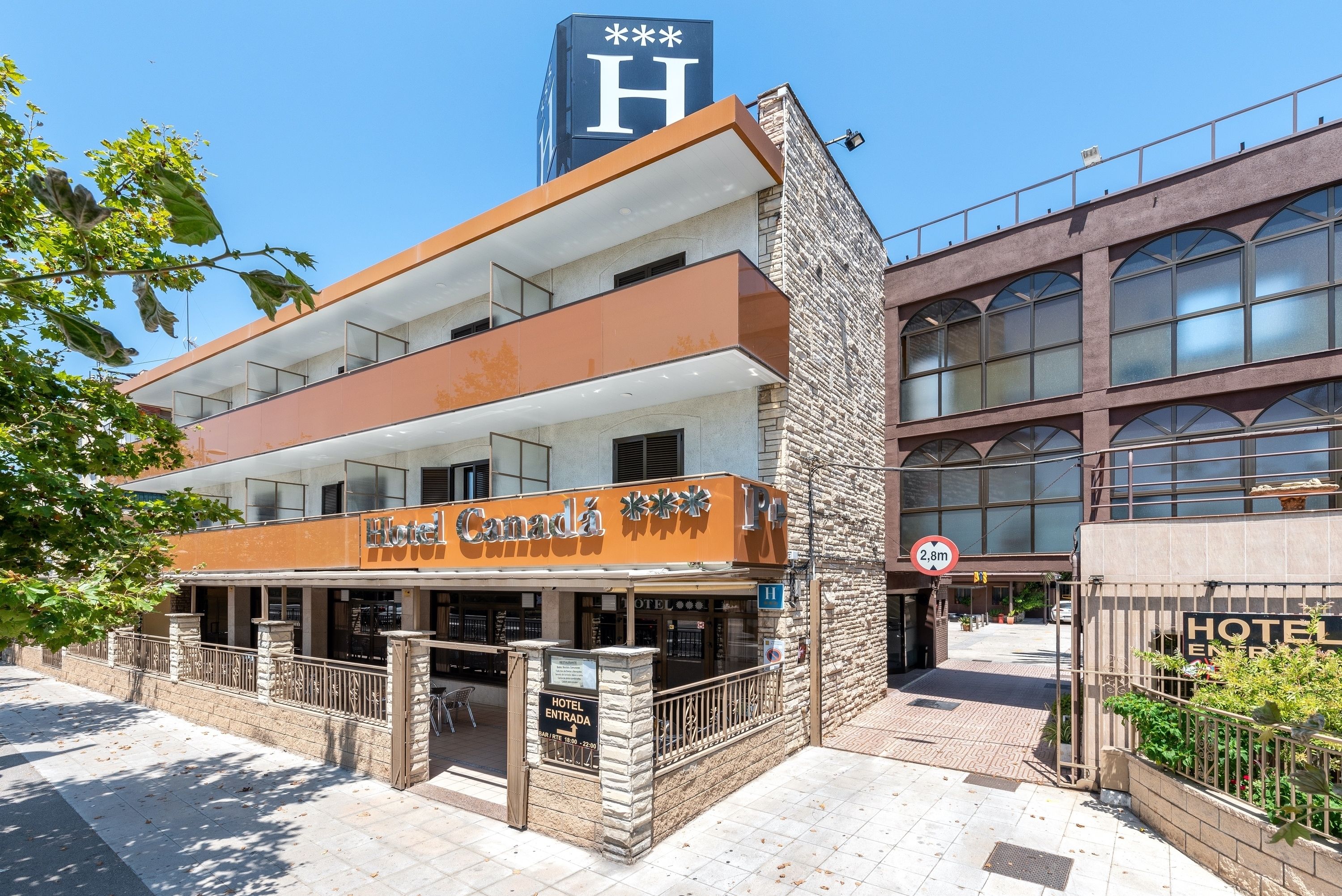 Hotel amb façana moderna, un senyal prominent amb la lletra 'H' i una indicació de límit d'alçada de 2,8 metres.
