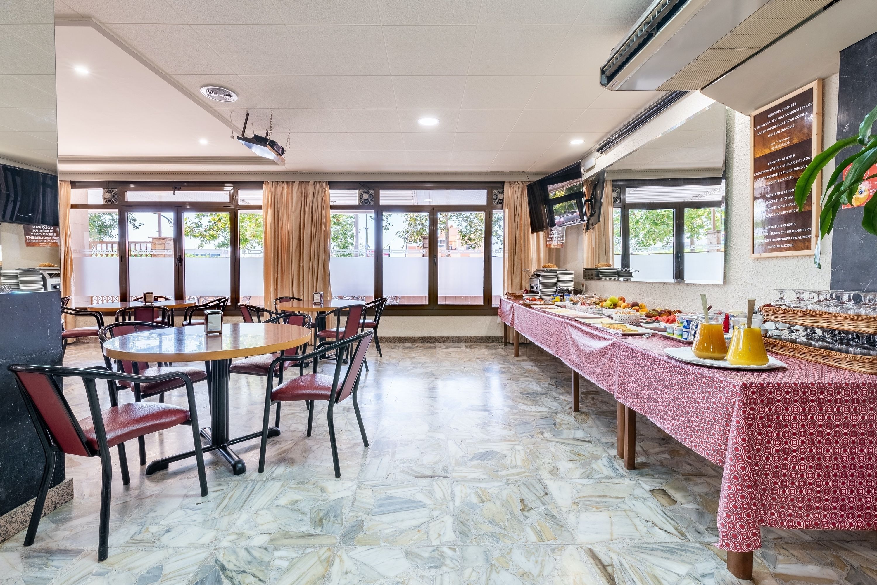 Een eetgedeelte met een marmeren vloer, ronde tafels en stoelen. Er is een buffettafel met eten en drinken.